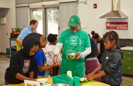 Photo of program educator with students in cooking classroom. 