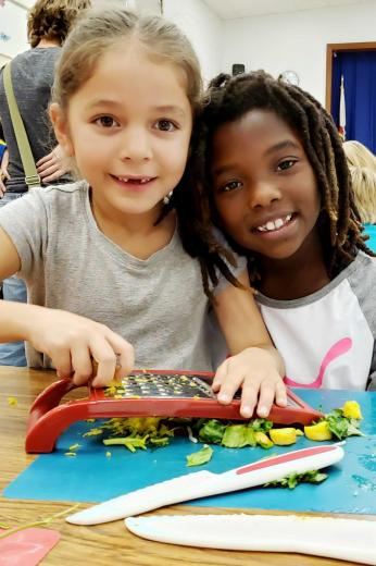 Kids using grater to shred carrot